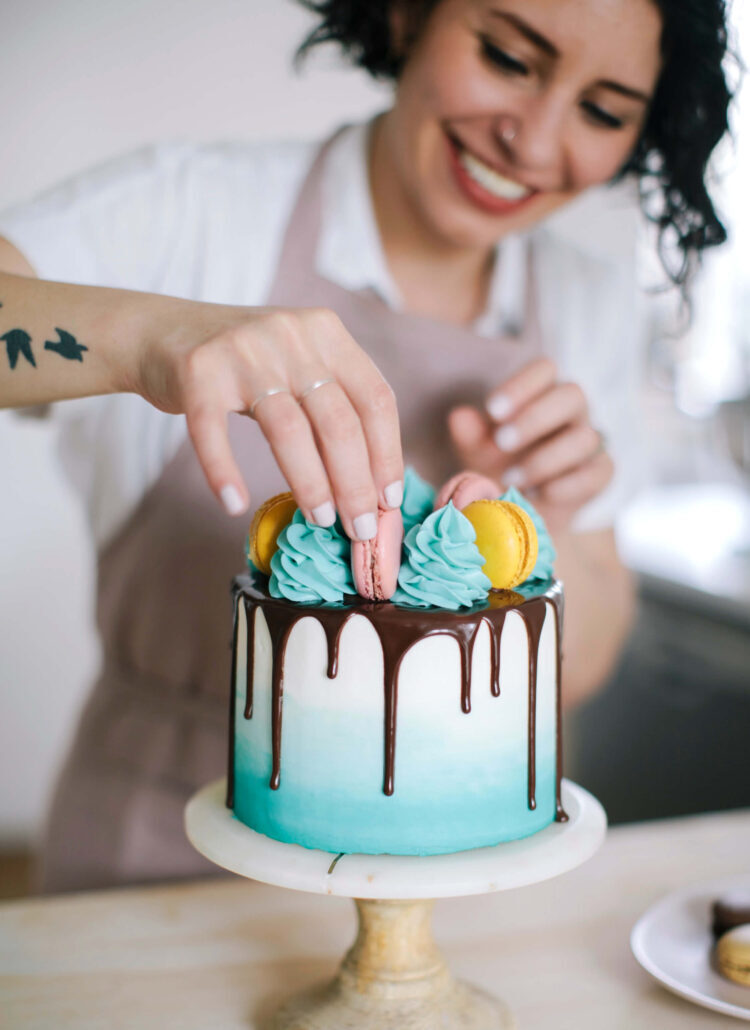 Whitney DePaoli places a decoration on a blue and white cake with a chocolate drip