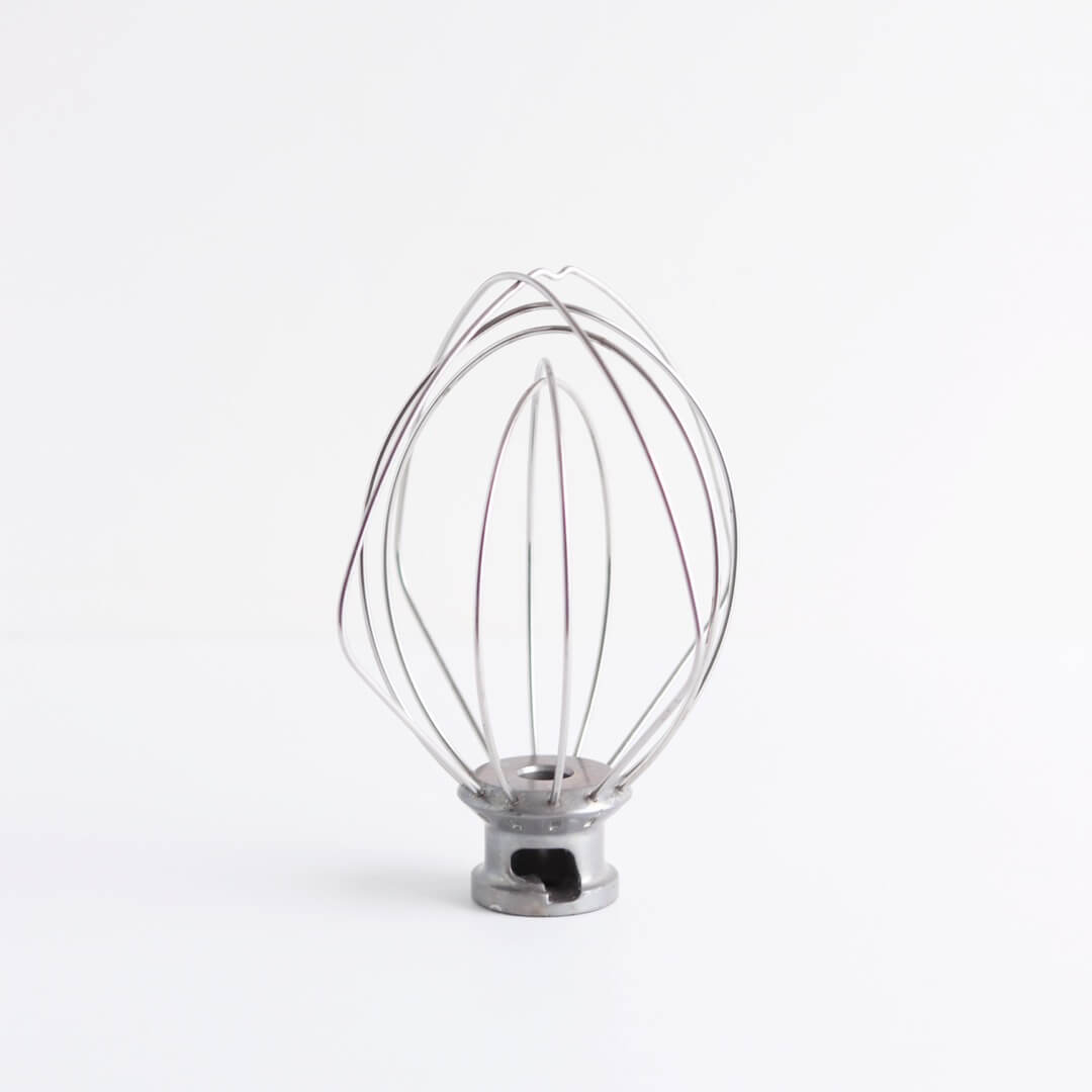 A KitchenAid whisk attachment sits on a white background.