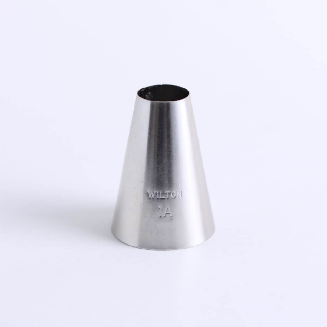 A metal icing tip (Wilton Tip 1A) sits on a white background.