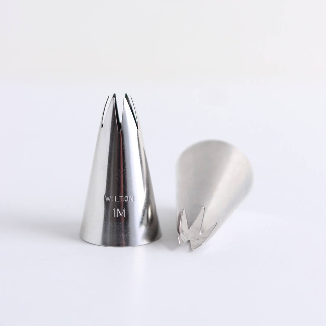 A metal icing tip (Wilton tip 1M) sits on a white background.